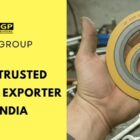 A hand holds stacked yellow and gray gaskets with "IGP" branding in a workshop. Text reads "Most Trusted Gaskets Exporter in India" on a bright yellow background. Tools and a glove are visible.